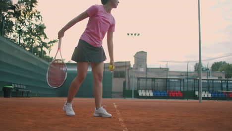Low-angle-view-in-slow-motion-of-a-young-female-tennis-player-preparing-to-serve-a-tennis-match.-A-woman-athlete-is-powerfully-hitting-a-ball-during-sports-practice.-Commercial-use-footage
